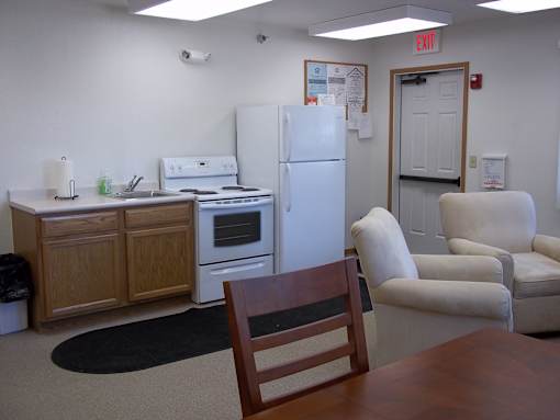 A kitchen with a refrigerator, oven, and a table with a chair.