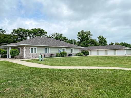 A house with a grey roof and a green trash can in front of it.