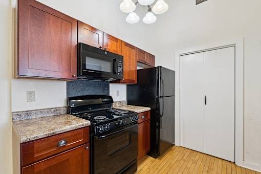 A kitchen with a black refrigerator, black stove, and wooden cabinets.