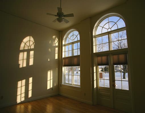 A room with a ceiling fan and large windows letting in sunlight.