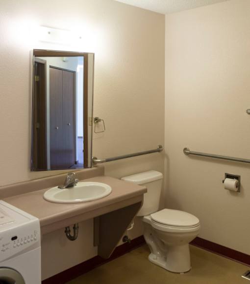 A bathroom with a toilet, sink, mirror, and washer.