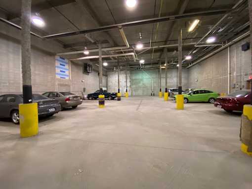 A parking garage with cars parked and yellow bollards.