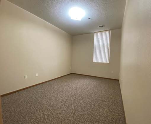 A room with a carpeted floor and a window with blinds.