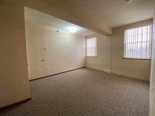 A room with carpeted floor and a window with blinds.