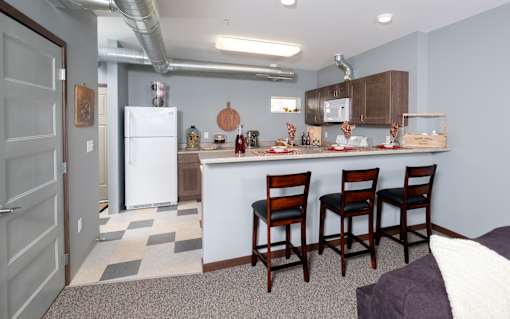 A kitchen with a white fridge and wooden chairs.