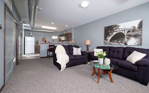 A living room with a black couch, a coffee table, and a painting on the wall.