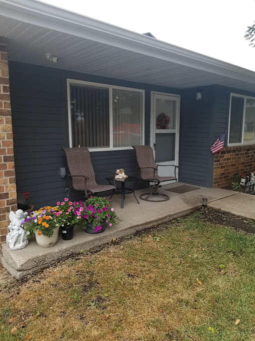 A house with a blue siding and a porch with two chairs and a table.