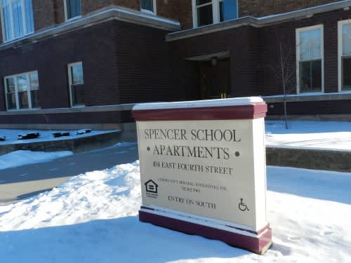 A sign for Spencer School Apartments sits in the snow.