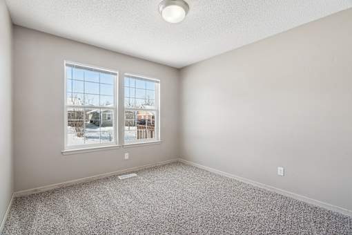 A room with a grey carpet and two windows overlooking a snowy landscape.