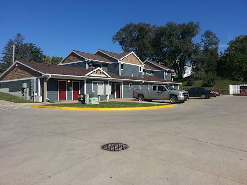 A building with a grey roof and a red door is surrounded by a parking lot.