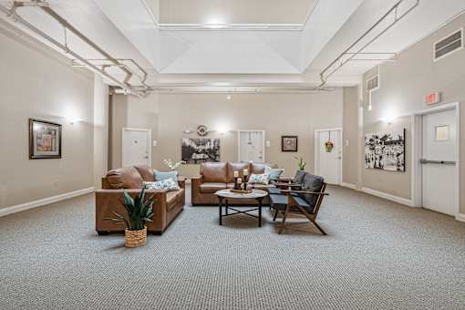 A living room with a brown couch, a chair, and a table with a vase of flowers on it.