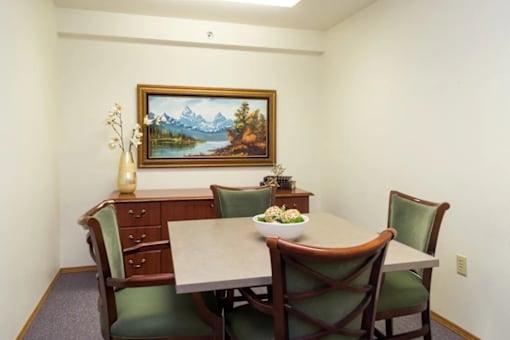 A painting of a mountain scene is on the wall above a table with chairs around it.