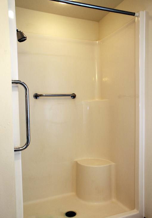 A white shower stall with a black grab bar.