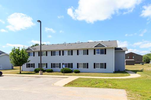 A white building with a grey roof and a parking lot in front.