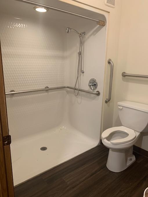 A white toilet is mounted above a white bathtub with a shower head.