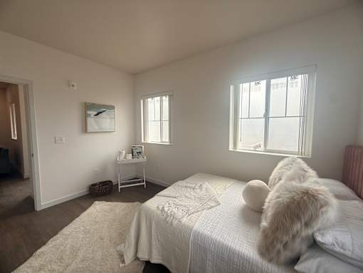 A white bedroom with a bed, a small table, and a window.