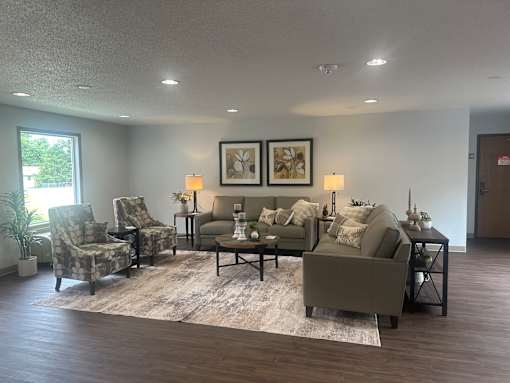 A living room with a grey couch, two chairs, a coffee table, and two framed pictures on the wall.
