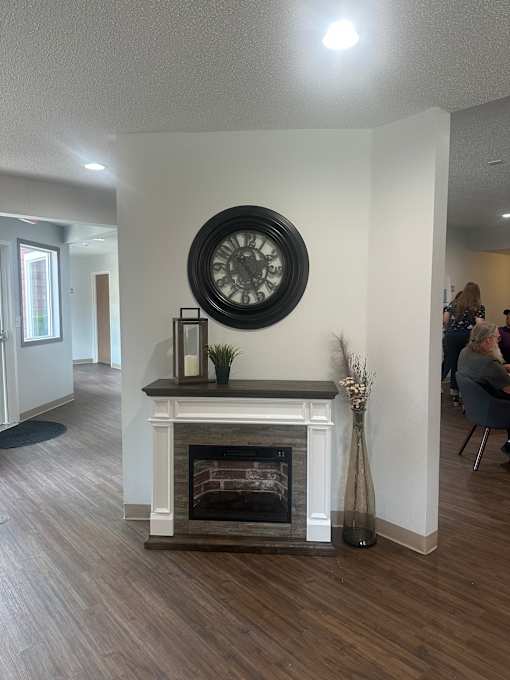 A clock hangs on a wall above a fireplace in a room.
