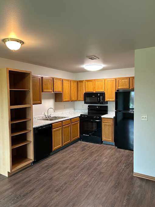 A kitchen with wooden drawers and a black fridge.
