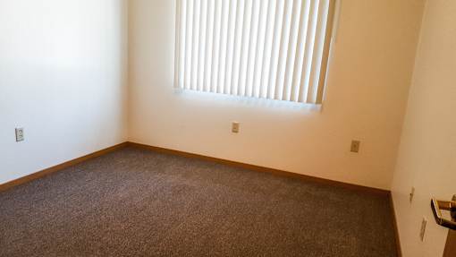 A room with a carpeted floor and a window with blinds.