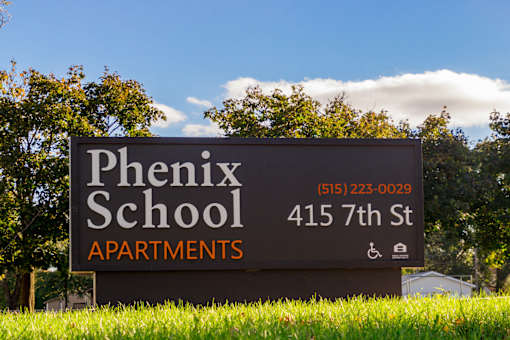 A sign for Phoenix School Apartments is displayed in front of a tree.