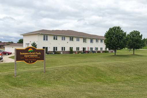 A sign for Summerfield Park Apartments stands in front of a white building.