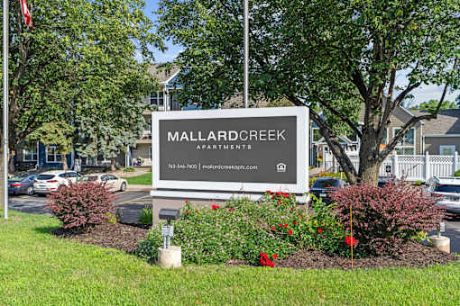 A sign for Mallard Creek Apartments is surrounded by flowers and greenery.