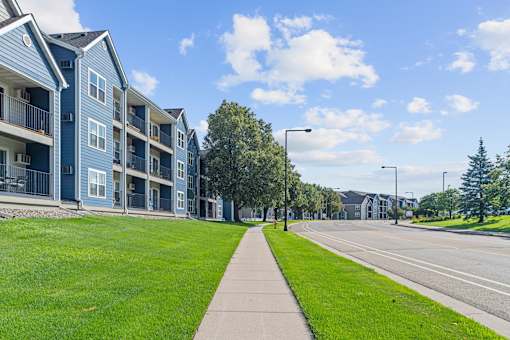A long grassy area with a sidewalk and apartment buildings on the left.