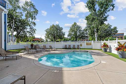 A small pool surrounded by a white fence and chairs.