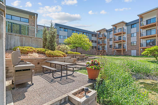 A patio with a table and chairs is surrounded by a garden and apartment buildings.