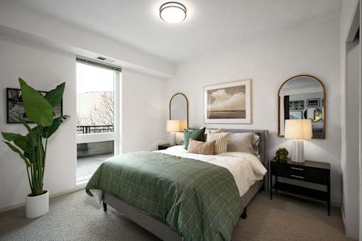 A bedroom with a bed, nightstand, and a plant.