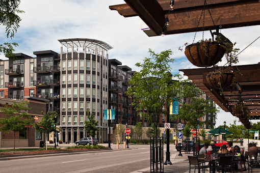 A street view of a city with a building in the background and people sitting at tables under a canopy.