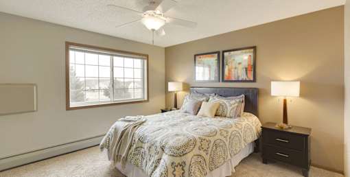 A bedroom with a bed, two lamps, and a ceiling fan.