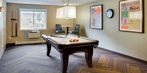 A pool table is in the middle of a room with a window and a chair.