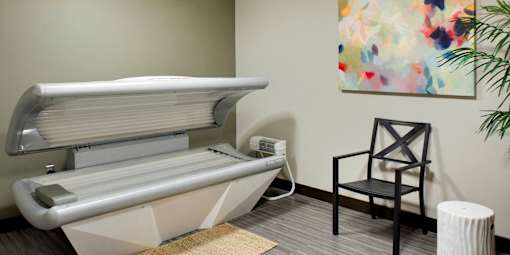 A tanning bed in a room with a chair and a plant.