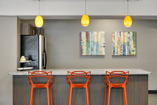 A kitchen with a refrigerator, two chairs and two paintings hanging on the wall.