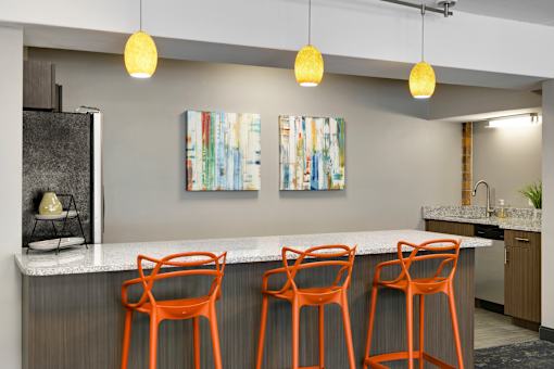A kitchen with a bar area featuring orange chairs and a white counter.