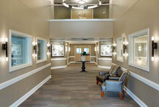 A hallway with a carpeted floor, a table with a vase, and chairs on either side.