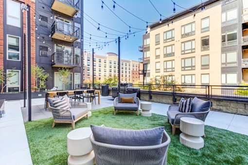 A patio with a white couch and chairs with a black railing and a building in the background.