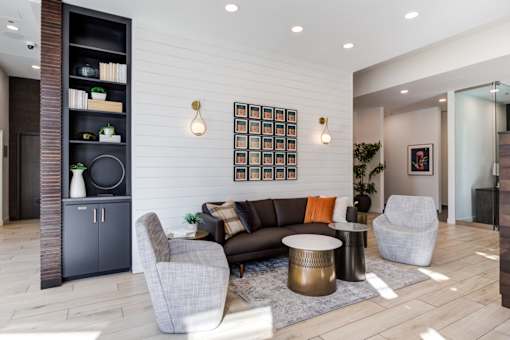 A modern living room with a grey sofa, a grey armchair, a black cabinet, and a wooden floor.