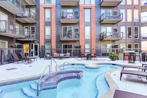 A pool with a metal railing is surrounded by chairs and tables.