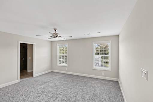 A room with a ceiling fan and two windows.