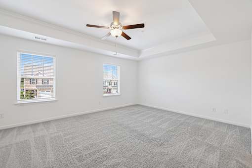 A room with a ceiling fan and two windows.