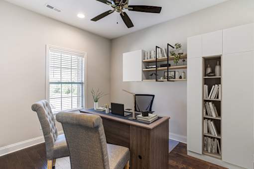 A room with a desk, chair, and a ceiling fan.