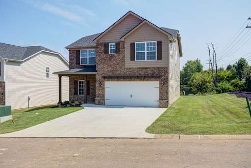 A two-story house with a garage is surrounded by a grassy area and a sidewalk.