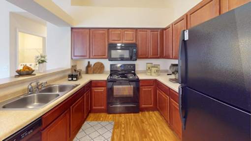 A kitchen with a black refrigerator, wooden cabinets, and a black stove top oven.