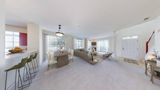 A well-lit, spacious living room with a dining area and a kitchen in the background.