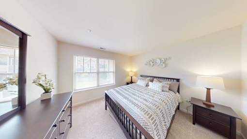 A bedroom with a large bed, a nightstand with a lamp, and a window with a view of the city.