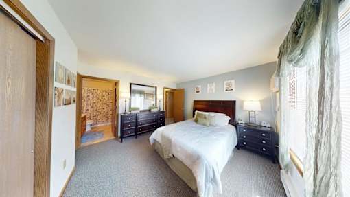 A bedroom with a large bed and a window with curtains.