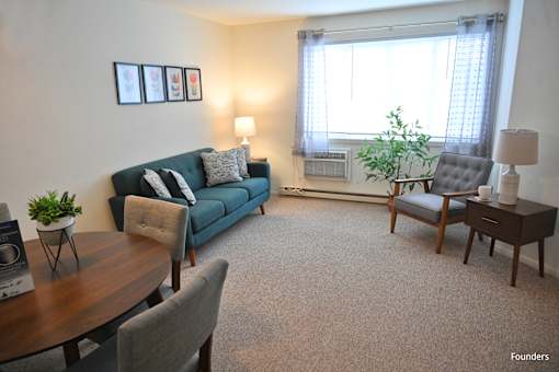 A living room with a blue couch, a grey armchair, a wooden table, and a carpet.